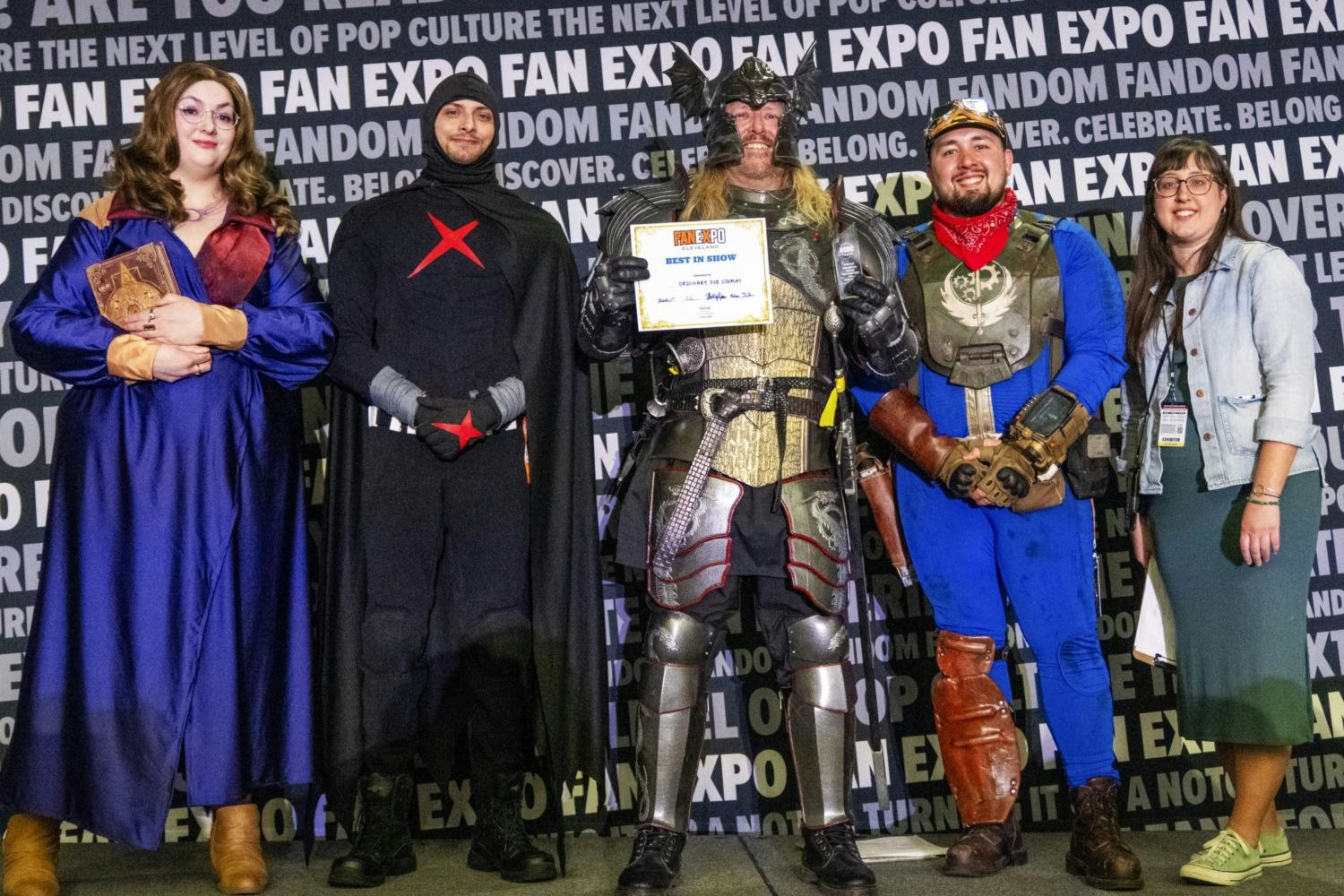 Five people stand in a row for a group photo. A heavily armored fantasy warrior in the center holds the “Best in Show” certificate. Judges stand around him, smiling proudly.