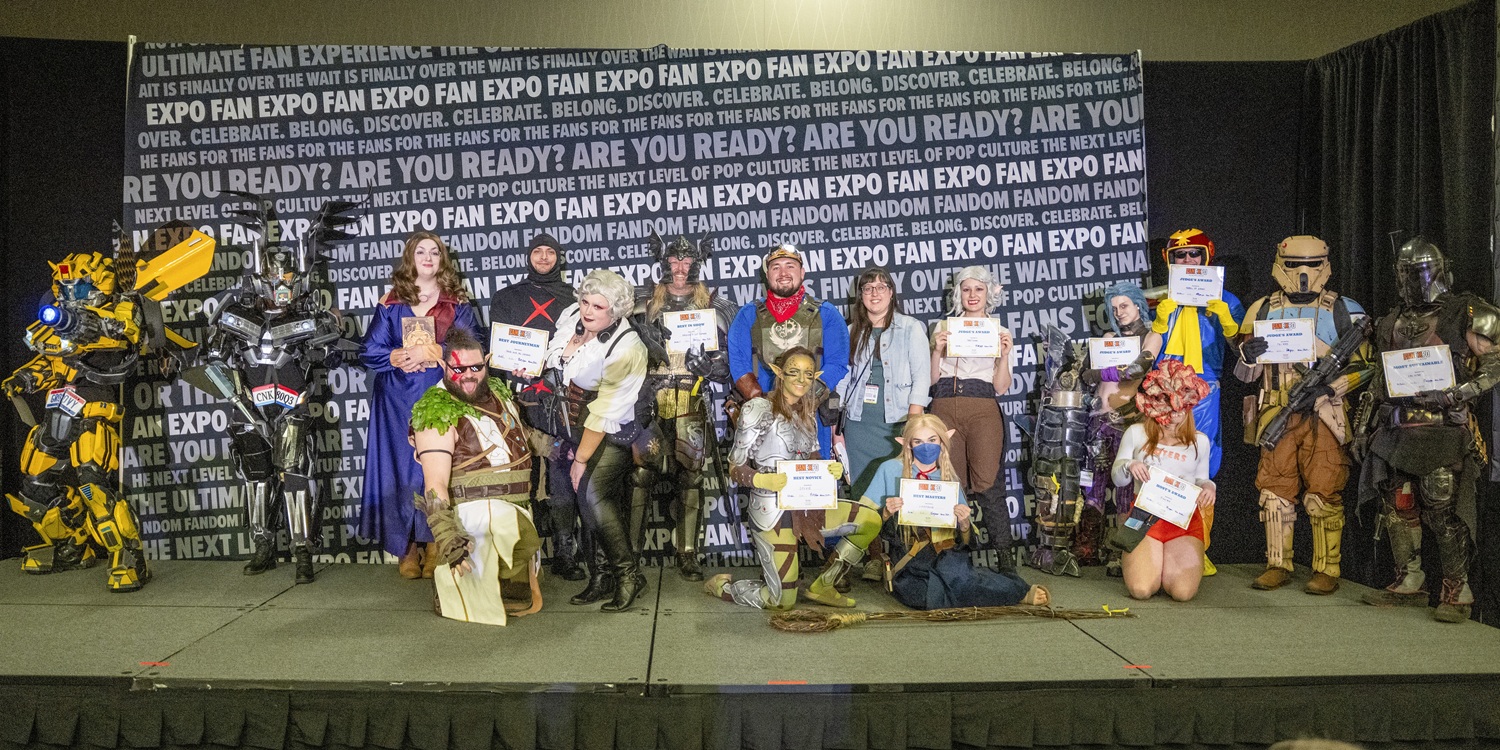 A large group of cosplayers pose together onstage at FAN EXPO Cleveland’s Cosplay Craftsmanship Cup. The backdrop behind them is covered with repeated FAN EXPO branding. The cosplayers showcase a wide mix of characters and genres, including armored sci-fi builds, fantasy heroes, video game characters, and pop-culture favorites. Many hold award certificates for categories like Best Novice, Best Master, and Best Group. Some wear full armor suits, others have elaborate props, wigs, or makeup, and a few kneel in the front row to display their costumes. The scene highlights the variety, creativity, and craftsmanship of the cosplay community at the show.