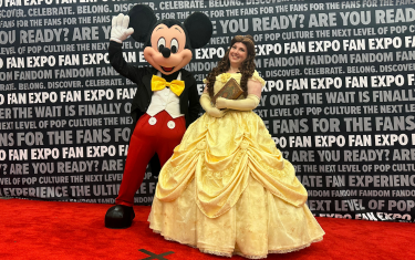Two cosplayers posing on the Cosplay Red Carpet. On the left is an adult dressed as Mickey Mouse, and on the right is a woman dressed as Belle from Beauty and the Beast.