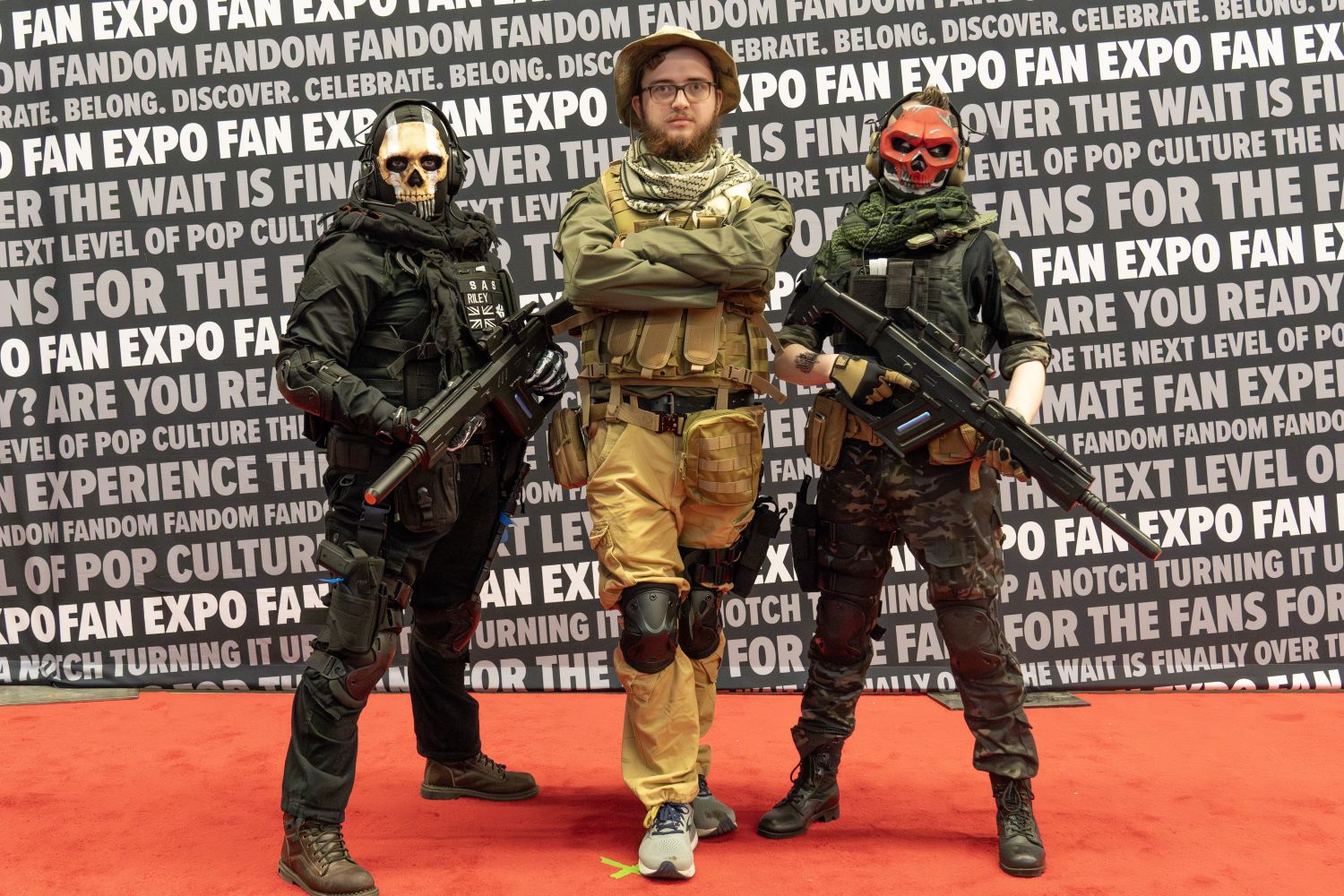A trio of cosplayers bring Call of Duty to life with military gear, tactical vests, and weapons. Two wear skull-face masks and pose in action-ready stances while the center figure stands stoically with arms crossed.