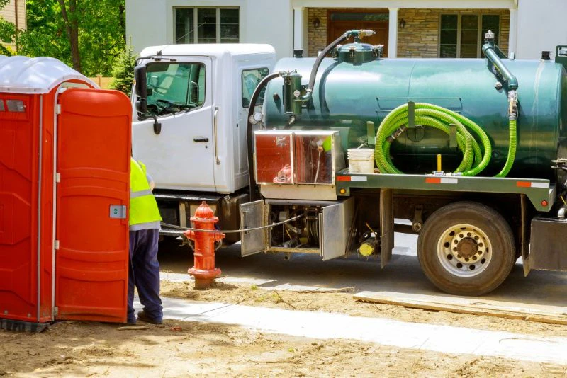 A portable restroom being emptied by a sanitation worker