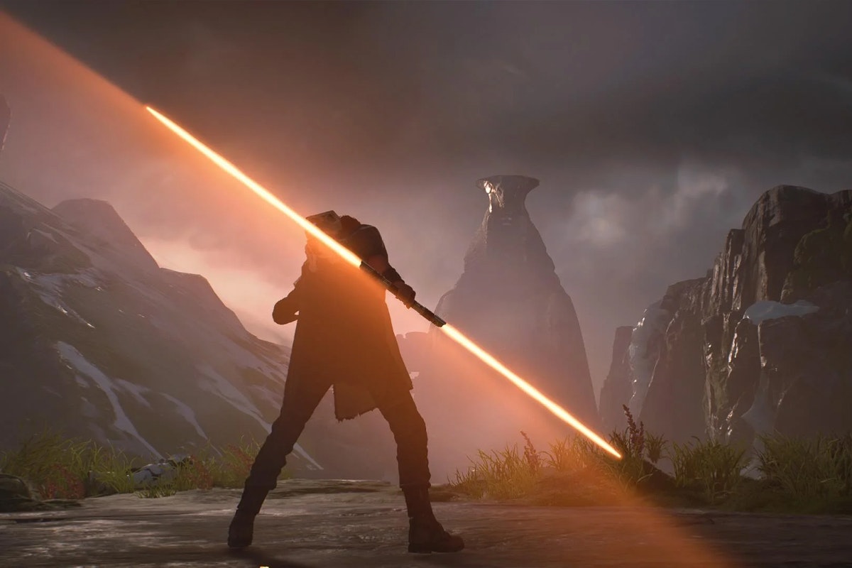A man in a poncho stands with back to camera holding a double bladed orange light saber with a mountain in the distance