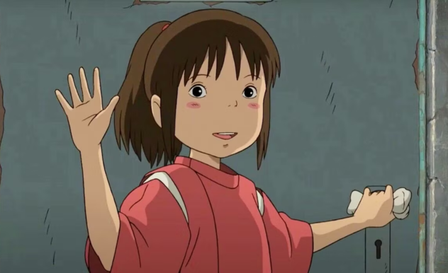 Leaving a building, Chihiro smiles and waves. Her opposite hand begins to turn the door handle with a cloth over it. She wears an oversized pink tunic and her hair is a high ponytail.