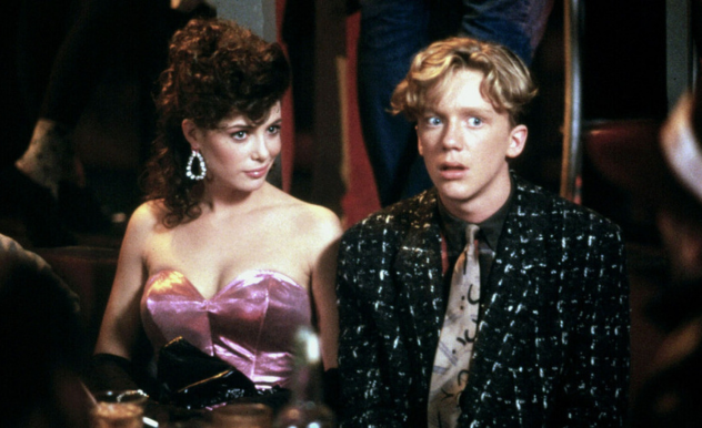 Gary and Lisa (Anthony Michael Hall, Kelly LeBrock) are seated at prom. Gary looks to be in awe as other students speak to him and his date.