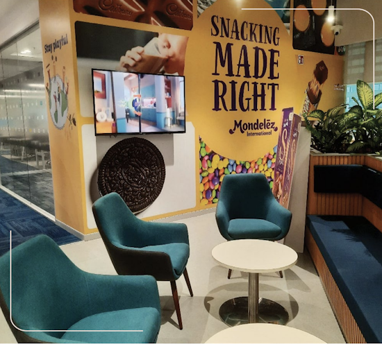 Booth with blue chairs and sofas, a display sign featuring cookies and treats, and a screen