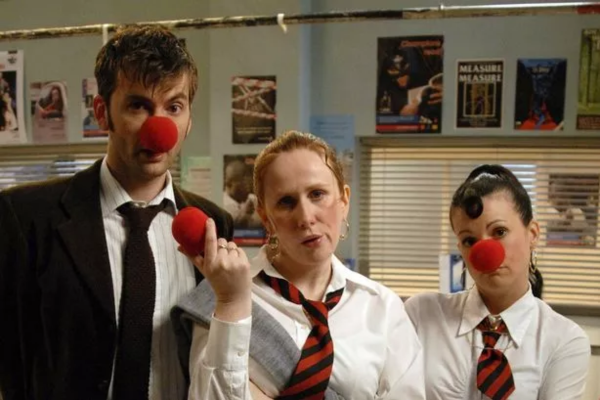 David Tennant (in a suit) with Cathrine Tate (in a prep school uniform) and another woman playing a girl (also in a prep school uniform) and they are wearing red clown noses.