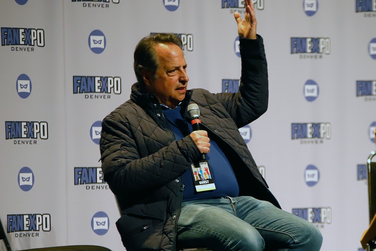 Jon Lovitz answers a question looking very seriously with his arm raised above his head