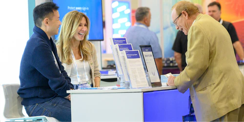 Three people standing at a trade show booth talking and laughing at Channel partners conference and expo.