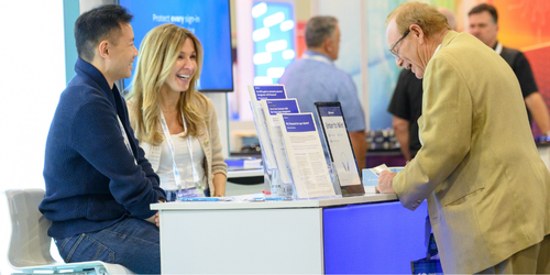 Three people standing at a trade show booth talking and laughing at Channel partners conference and expo.