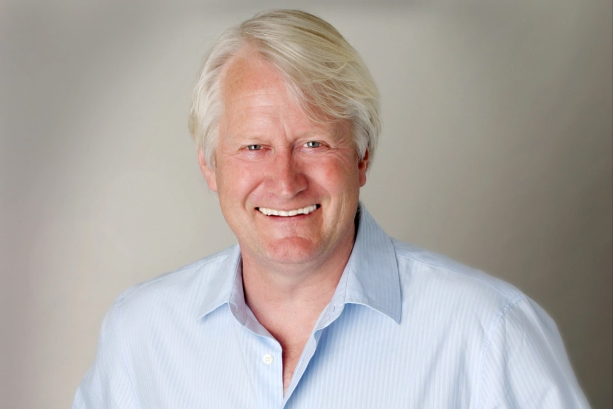 Charles Martinet smiles on a white backdrop with a blue collared shirt