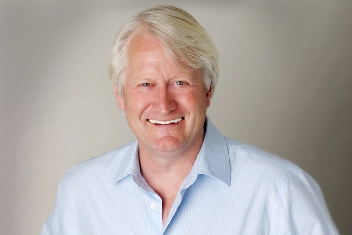 Charles Martinet smiles on a white backdrop with a blue collared shirt