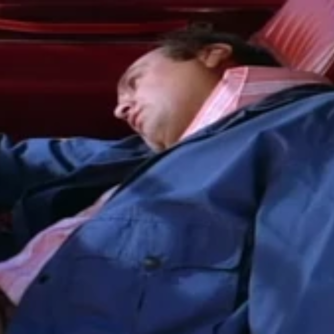 Charles Martinet, in a blue jacket and pink shirt, slumped to the side in a red seats of a car.