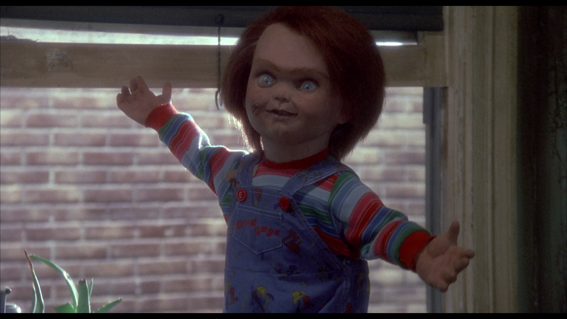 Chucky (doll, no cuts or injury) stands in Andy's window frame, his arms are extended as if to say "ta-da"