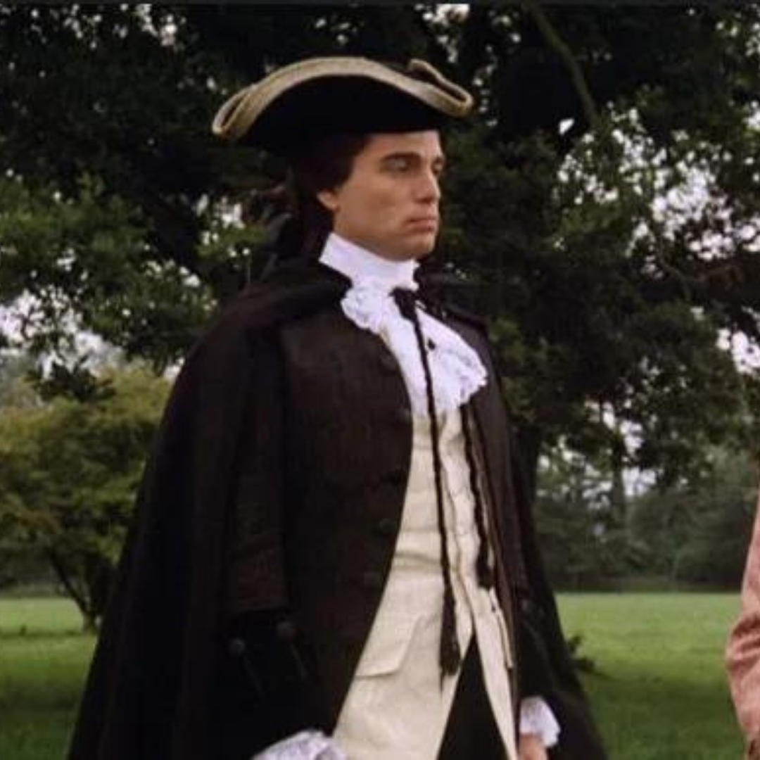 Chris Sarandon in a trifold hat and a old school suit and cloak.