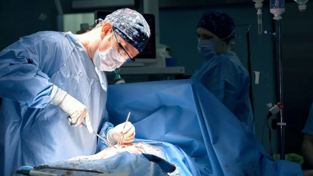 Cirurgião em centro cirúrgico realizando cirurgia oncológica acompanhado de assistente.