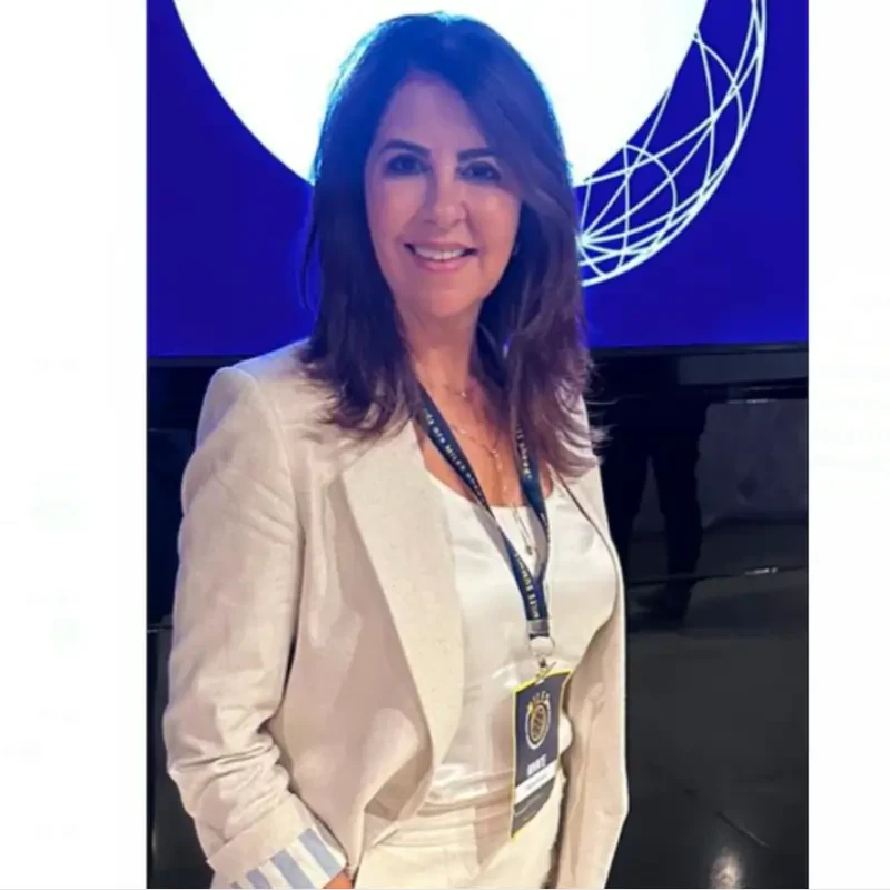 Claudia Herminia, palestrante no Healthcare Innovation Show, sorri usando blazer claro e crachá do evento.