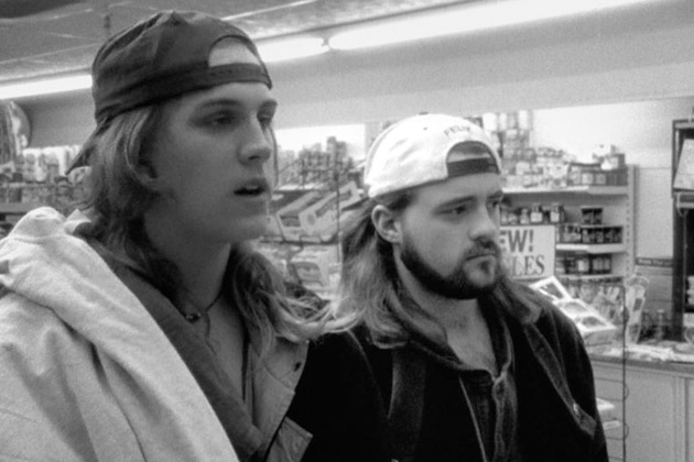 Jay Mewes as Jay and Kevin Smith as Silent Bob at a convenience store. The image is in black and white. Both are wearing their hats backwards and layered shirts and jackets. They are looking to the right of the image.