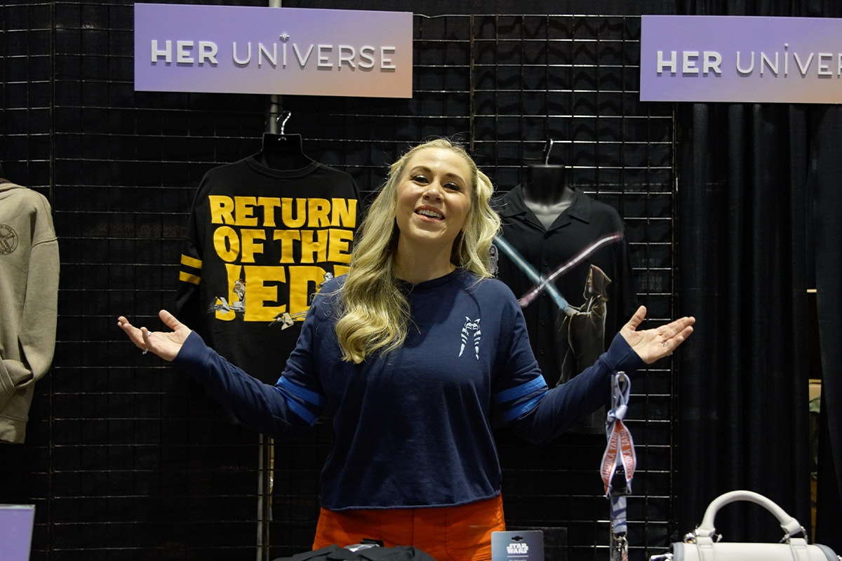 Ashley Eckstein stands with arms out at the HerUniverse booth