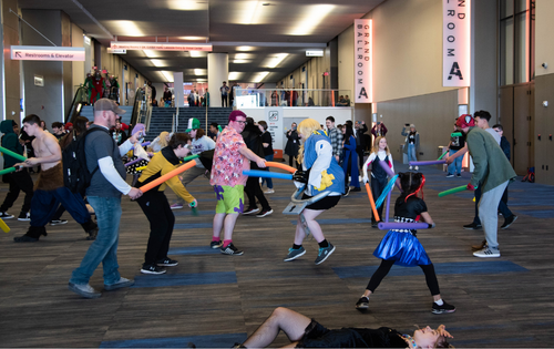 a group of adults and children having a lightsaber battle with foam lightsabers