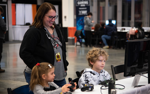 a mom watching her daughter and son play a video game on a computer