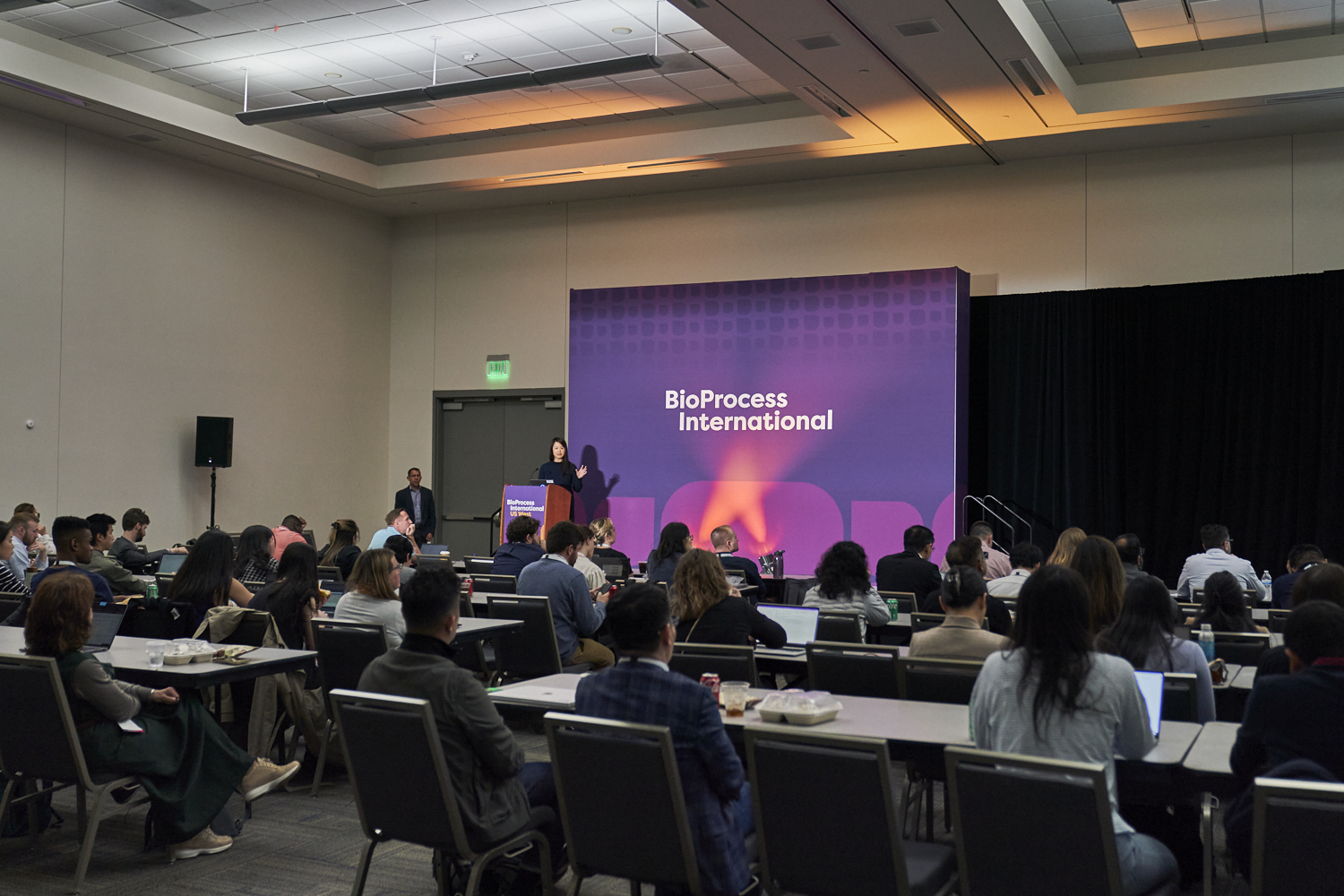 A conference room with attendees and a main speaker on stage at BPI West