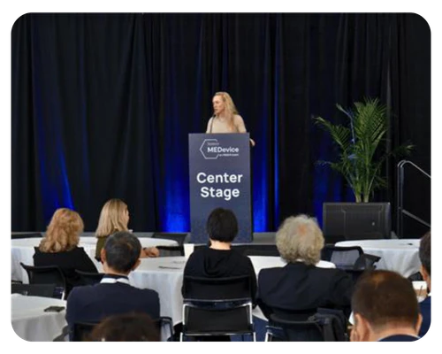 A woman giving a presentation at a conference, engaging with attendees while standing behind a podium
