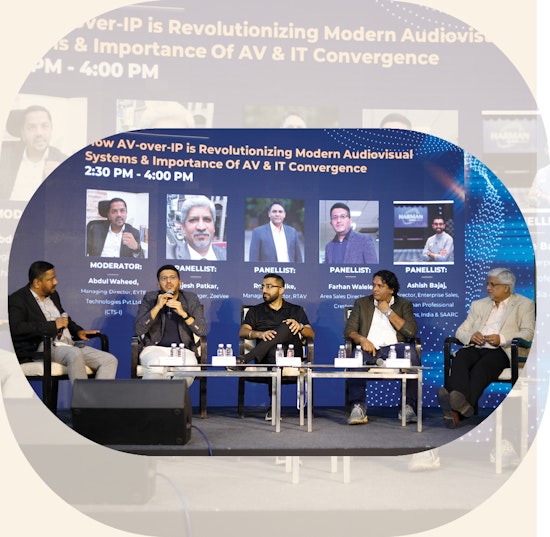 Panel discussion on AV-over-IP technology featuring five industry experts seated at a modern conference setup with headshots and titles displayed on backdrop screen