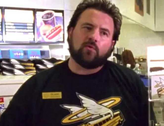 Kevin Smith in a convenience store. He is wearing a black shirt with a yellow school bus with wings and a halo.