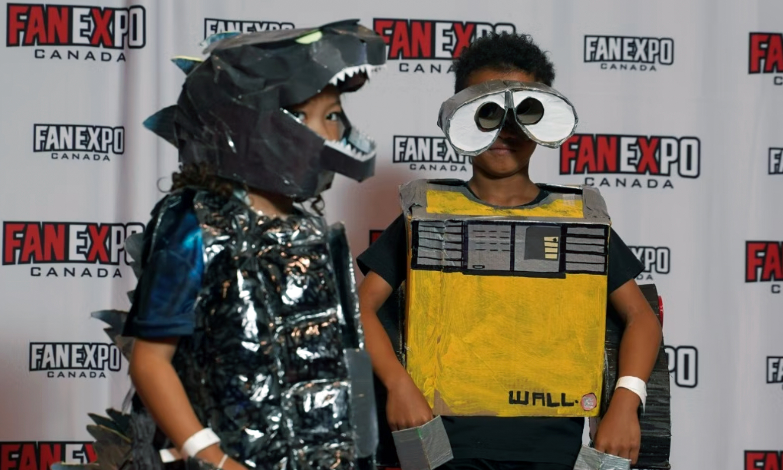 two young children pose on the red carpet in a dinosaur costume and a wall-e costume