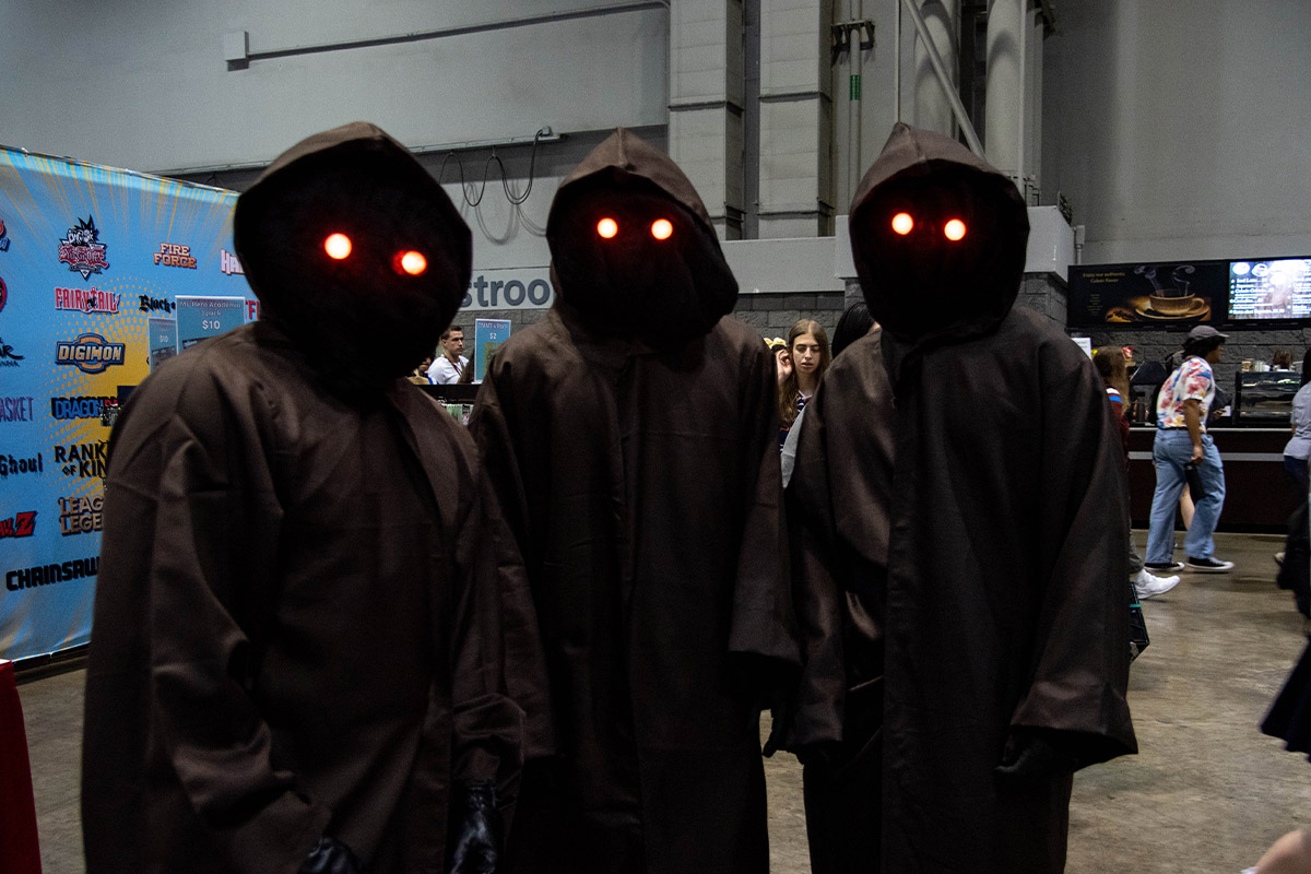A group of three Jawa's look at the camera with glowing yellow eyes