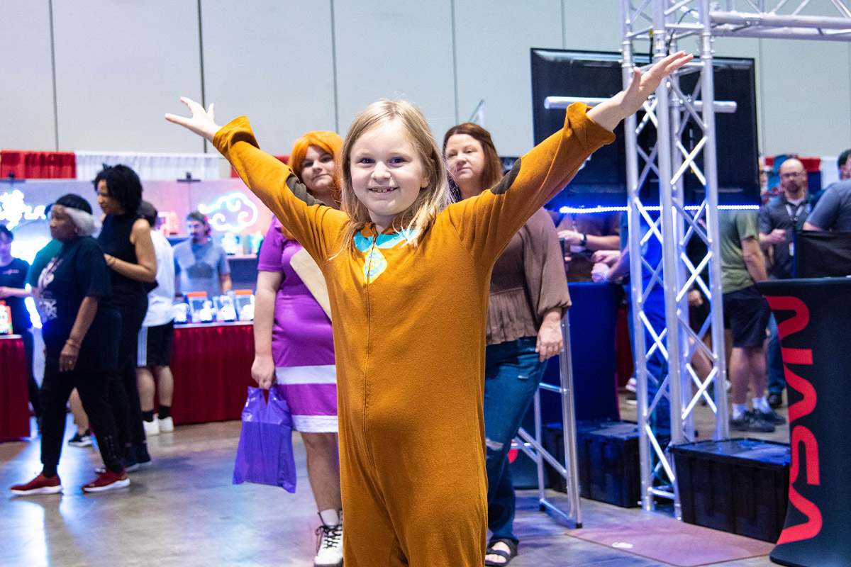 A young cosplayer wearing a Scooby Doo onsie smiles with arms stretched out