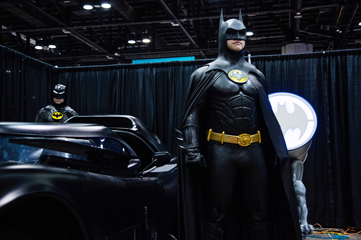 Batman poses heroically next to the Batmobile