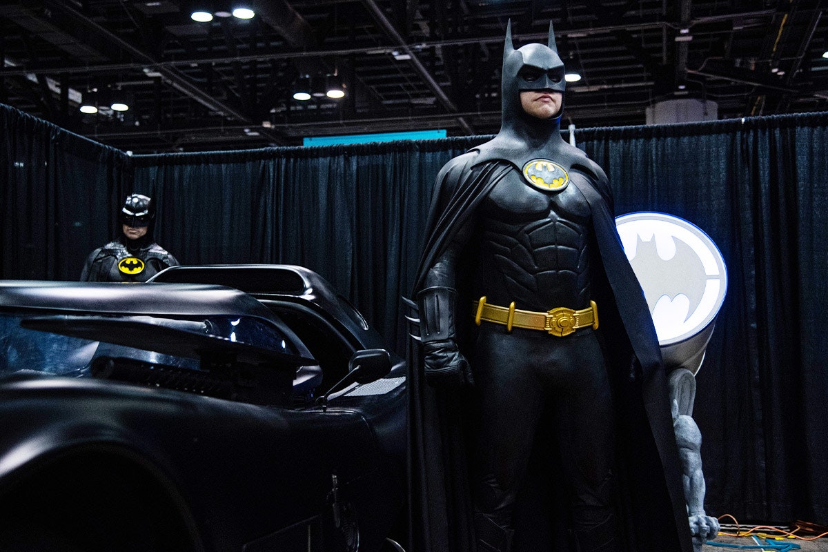 Batman poses heroically next to the Batmobile
