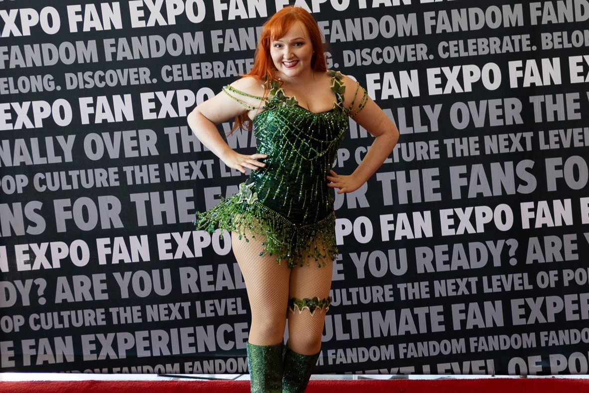 A cosplayer dressed as Poison Ivy, wearing a sparkly green costume with ivy decorations, posing confidently in front of the FAN EXPO step-and-repeat backdrop.
