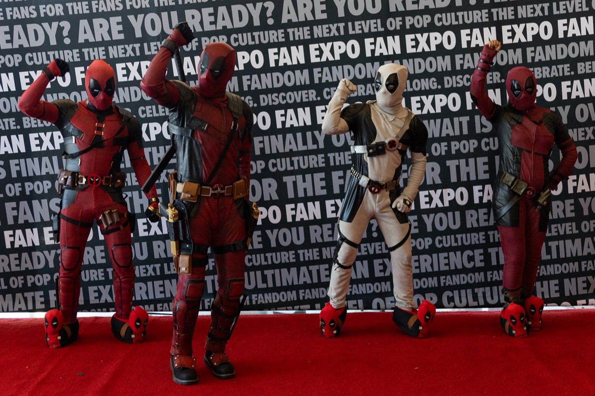 Four cosplayers dressed as Deadpool characters in various red and black or white costumes, posing humorously in front of a FAN EXPO backdrop.