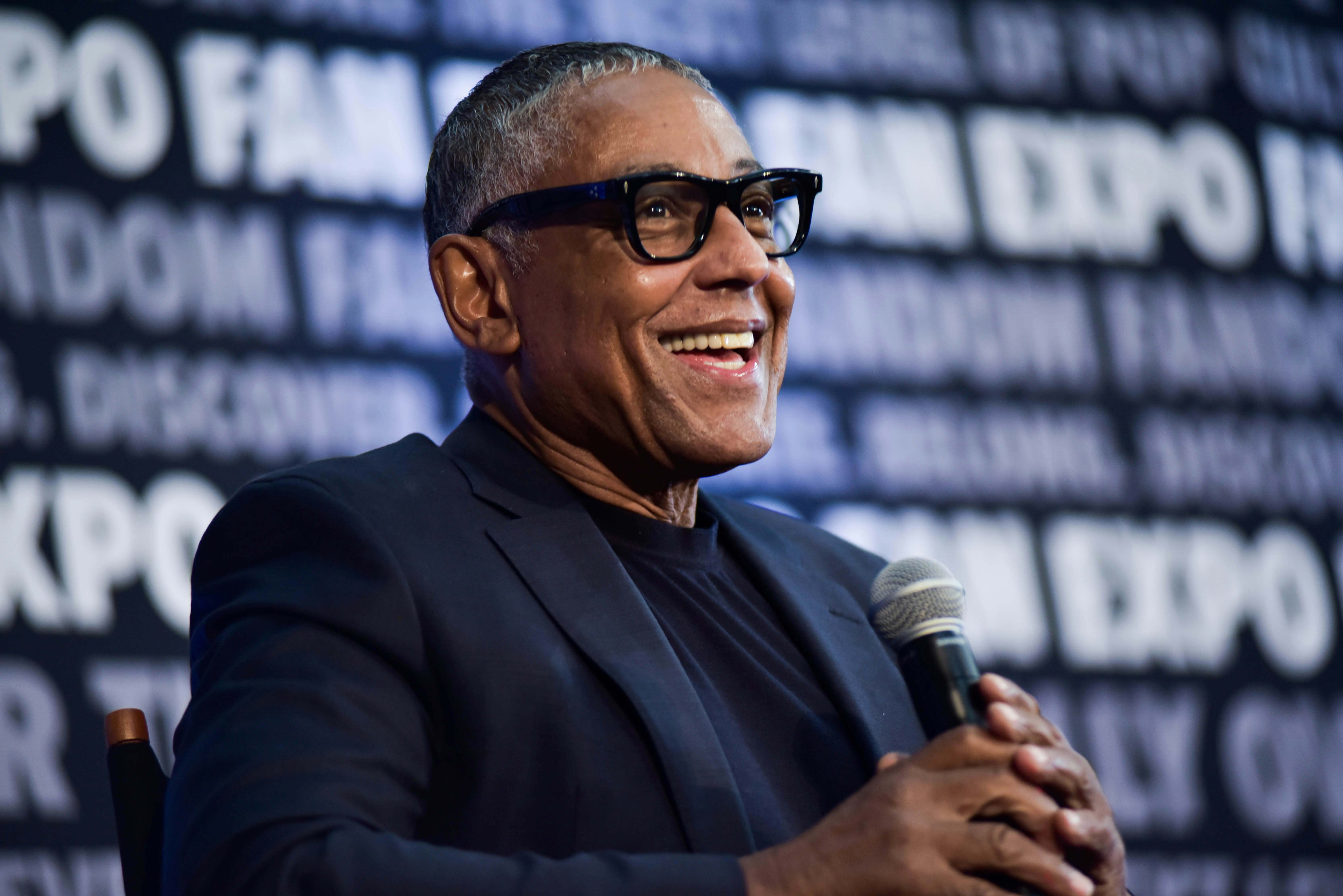 Giancarlo Esposito smiling at a fan's question during his panel, all while holding a microphone.