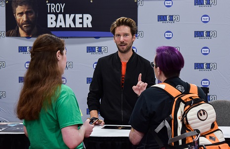 two women talking to voice actor Troy Baker at his table
