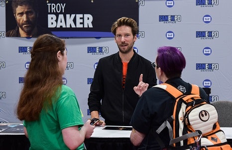 two women talking to voice actor Troy Baker at his table