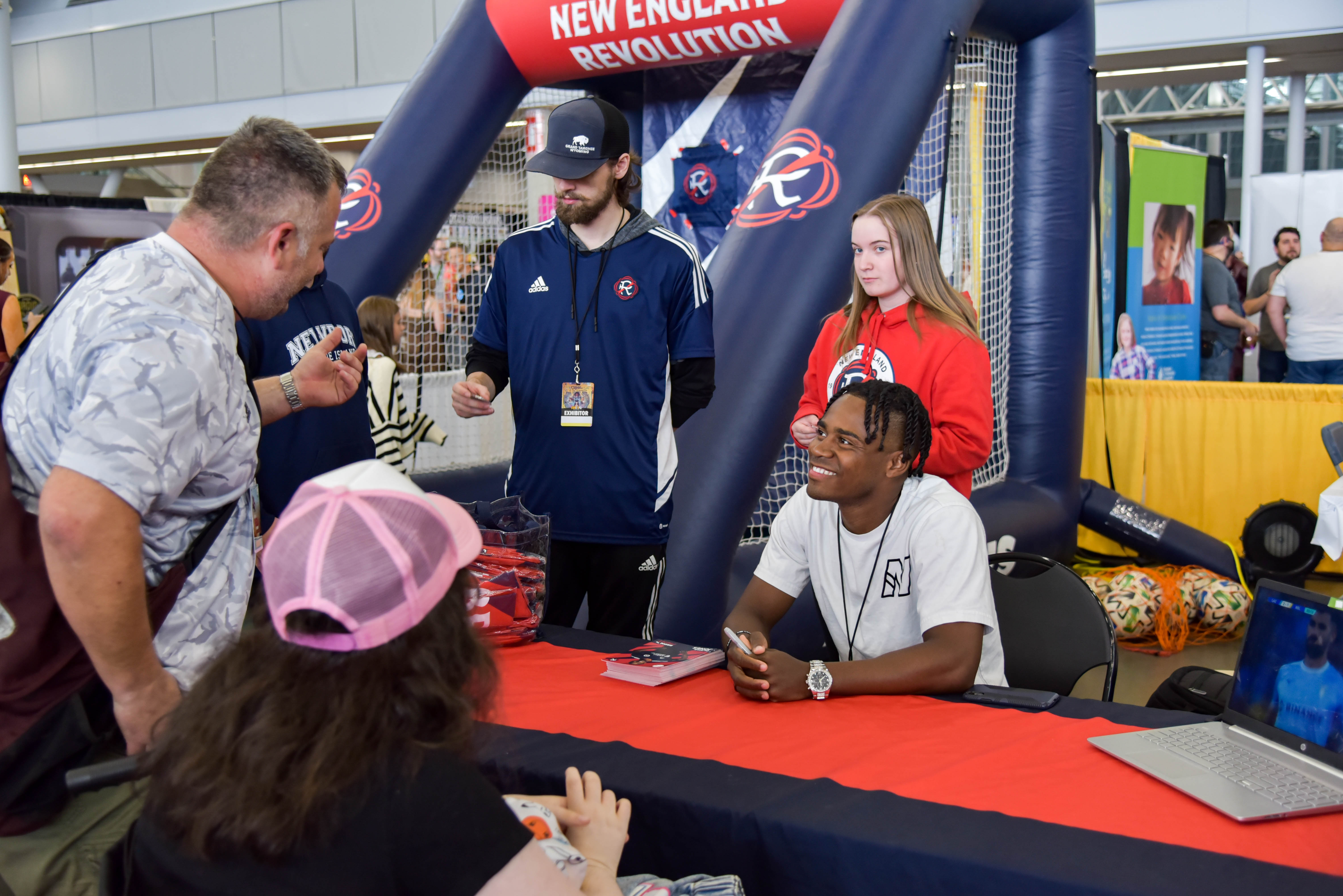 New England Revolution player DeJuan Jones smiling and meeting with some excited fans at his team's booth.
