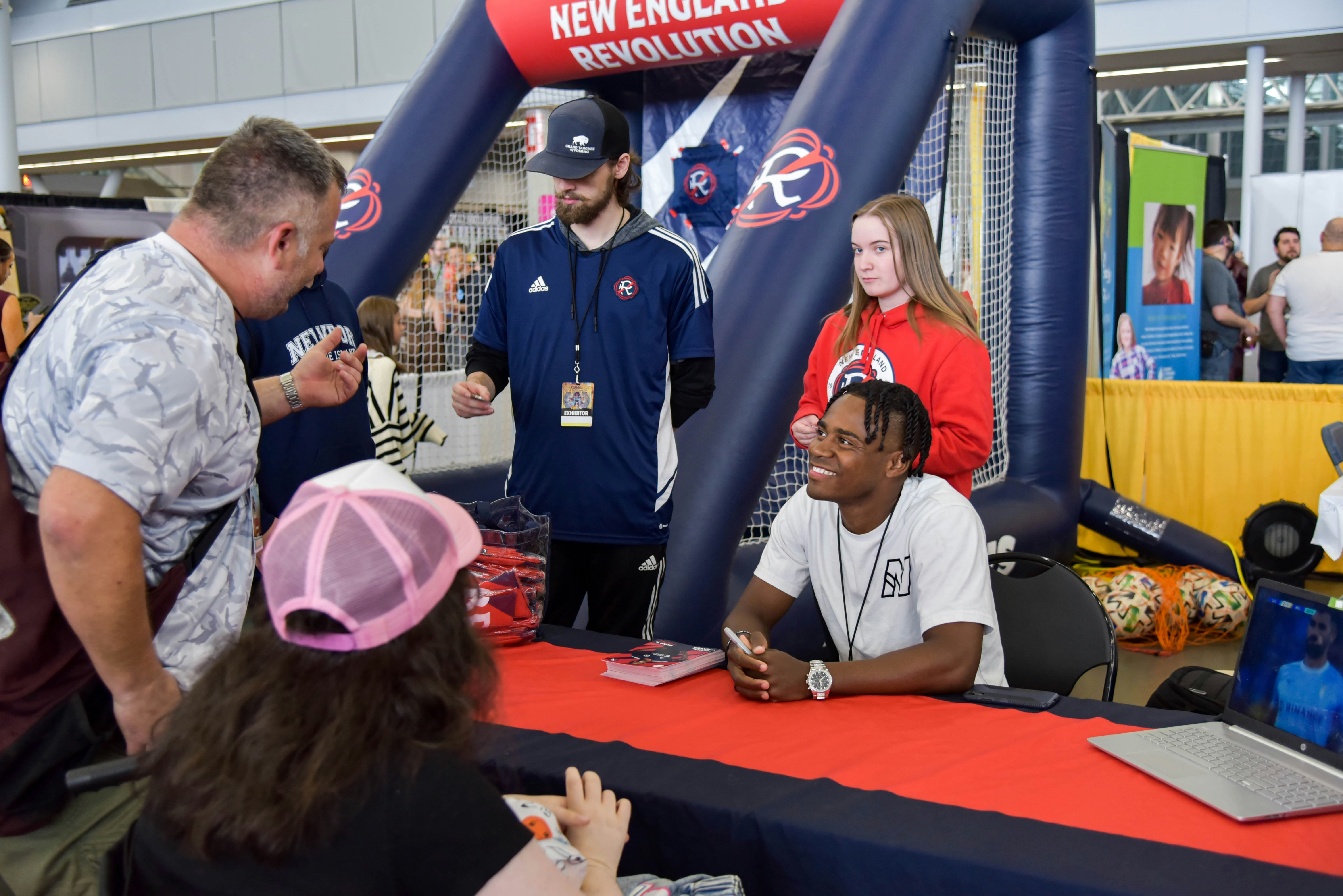 New England Revolution player DeJuan Jones smiling and meeting with some excited fans at his team's booth.
