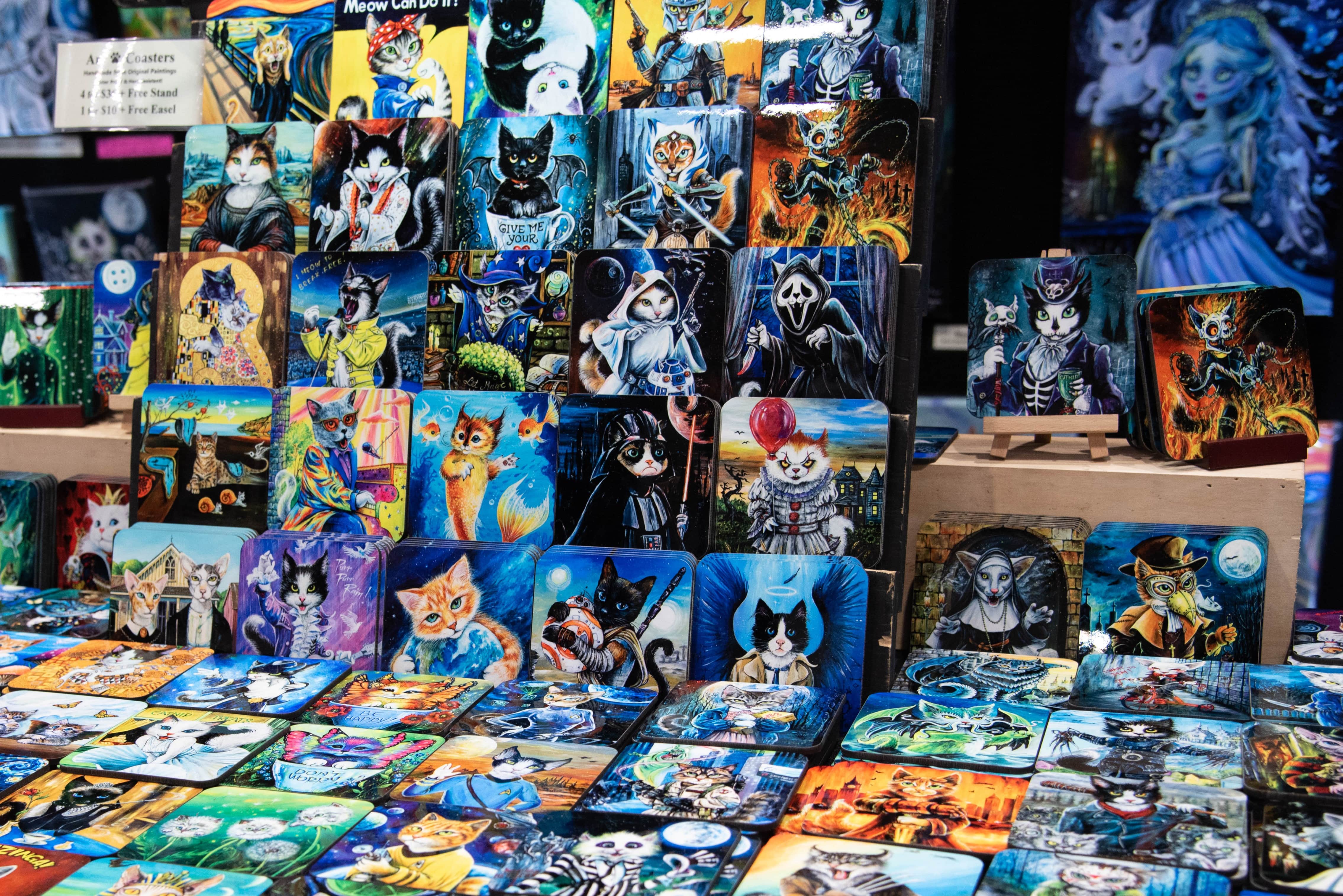 Some cat-based art on display at an artist alley booth, each with a different theme or fandom.