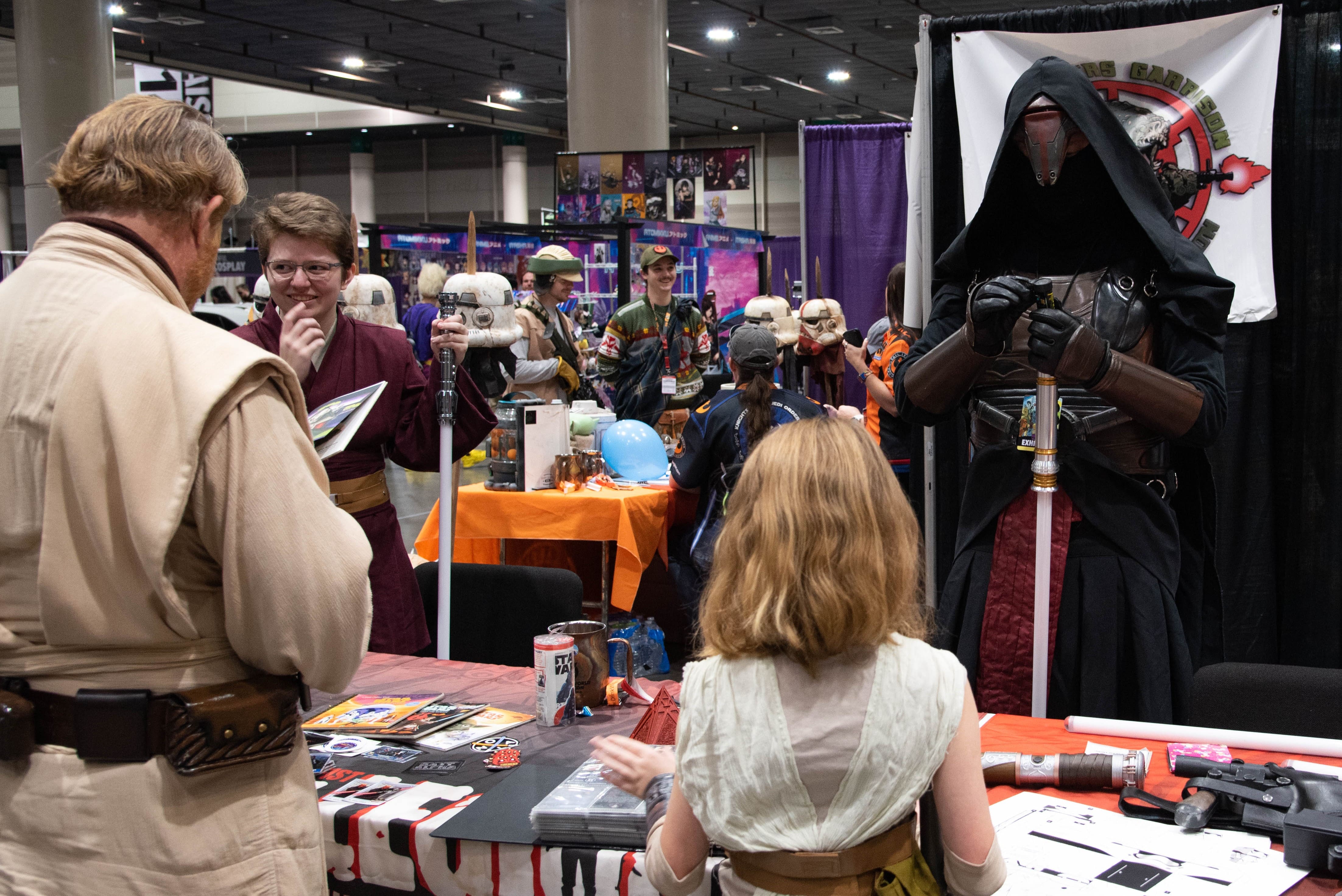 A shot from the 501st community booth, where a young Rey cosplayer interacts with Revan.