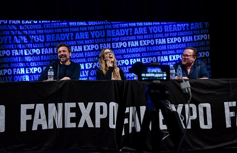 Will Friedle, Christy Carlson Romano, and Billy West sitting at a table with a "FAN EXPO" tablecloth, laughing and talking to each other.