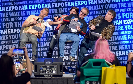 Dominic Monaghan, Elijah Wood, Billy West, and Sean Astin on stage, leaning right, reenacting being on the Millennium Falcon in Star Wars