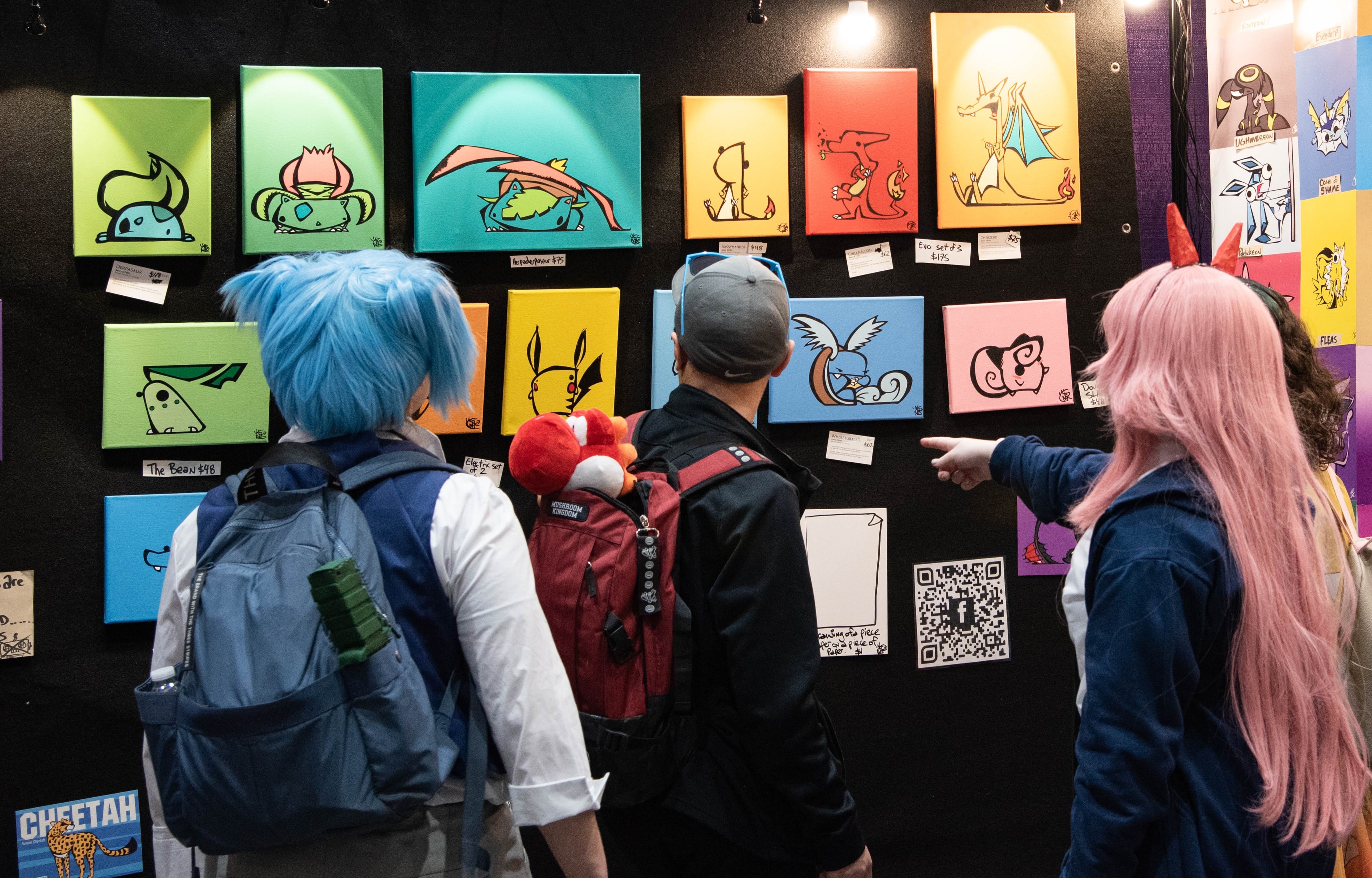 Several people browsing through canvas paintings at an artist alley booth.