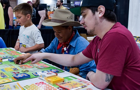 a man sitting at a table with two young boys, showing them the Pokémon trading game