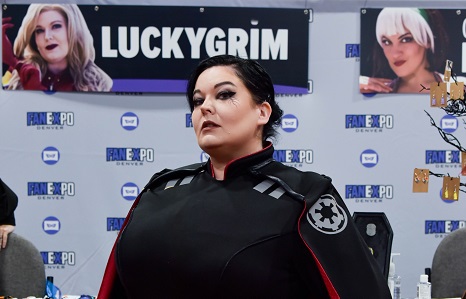 official cosplay guest, Luckygrim, standing in front of her Guest table, dressed in cosplay