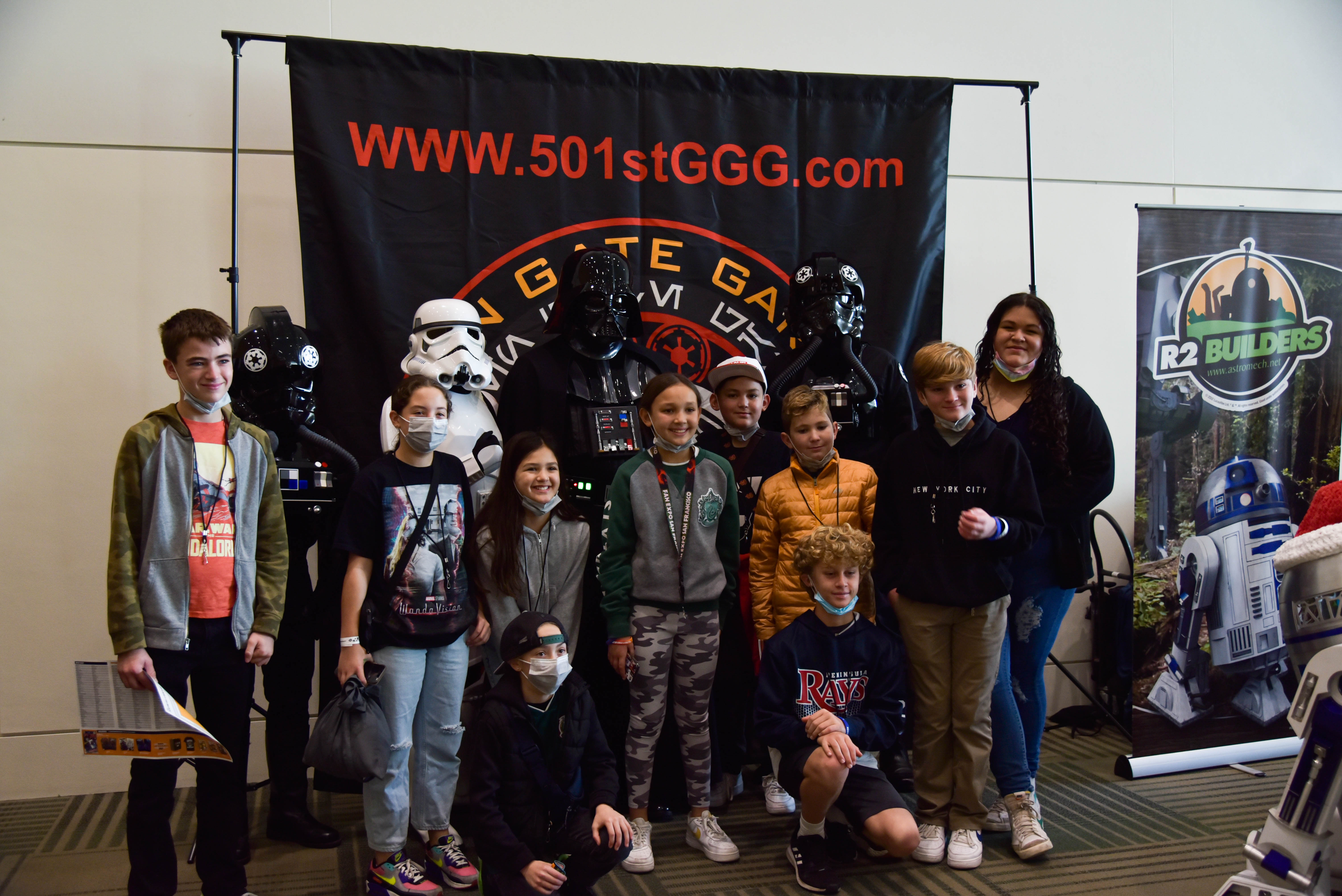 Group of kids posing for a picture with some Storm Troopers and Darth Vader