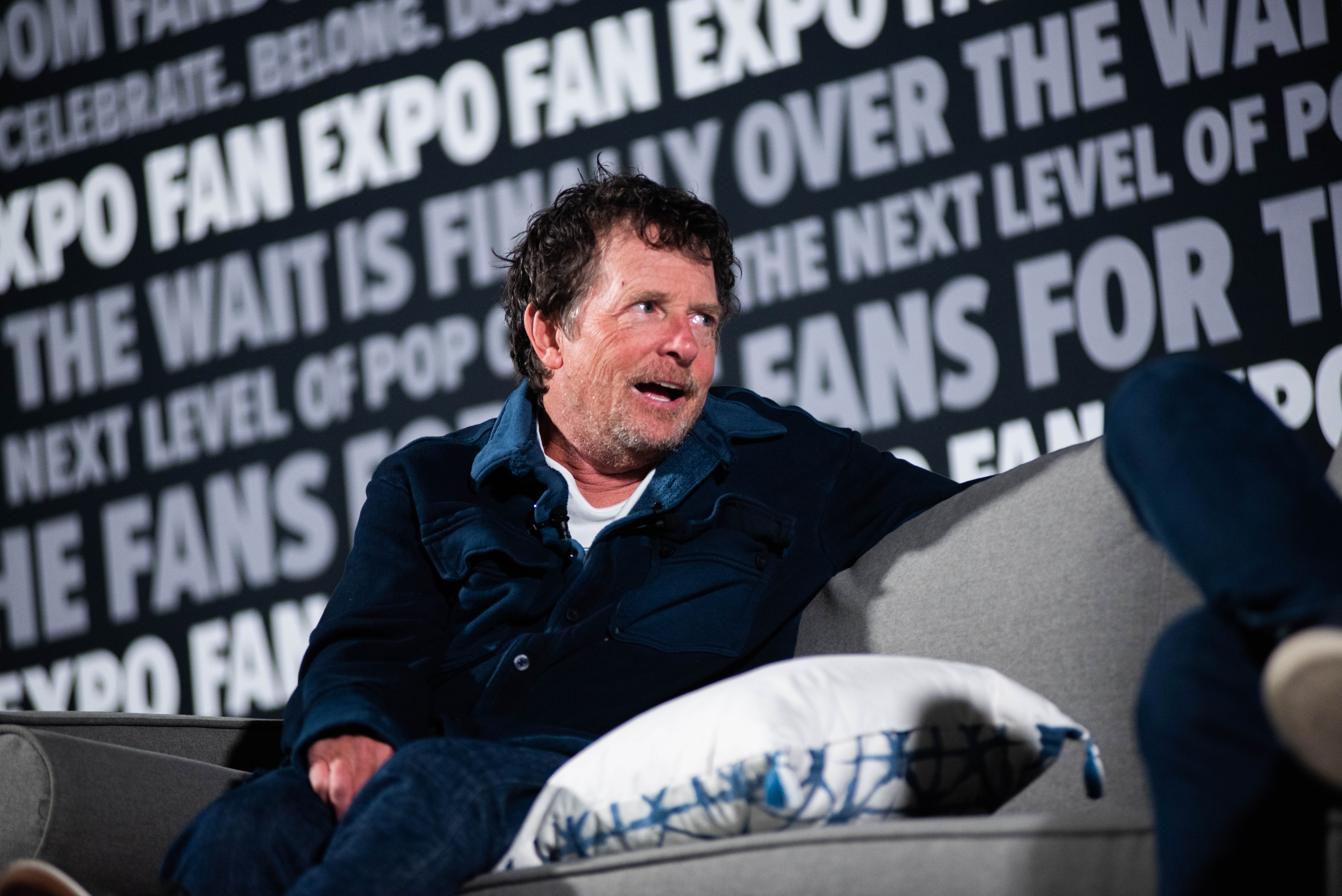 Michael J Fox say on a couch with Christopher Lloyd, smiling in the midst of answering fan questions
