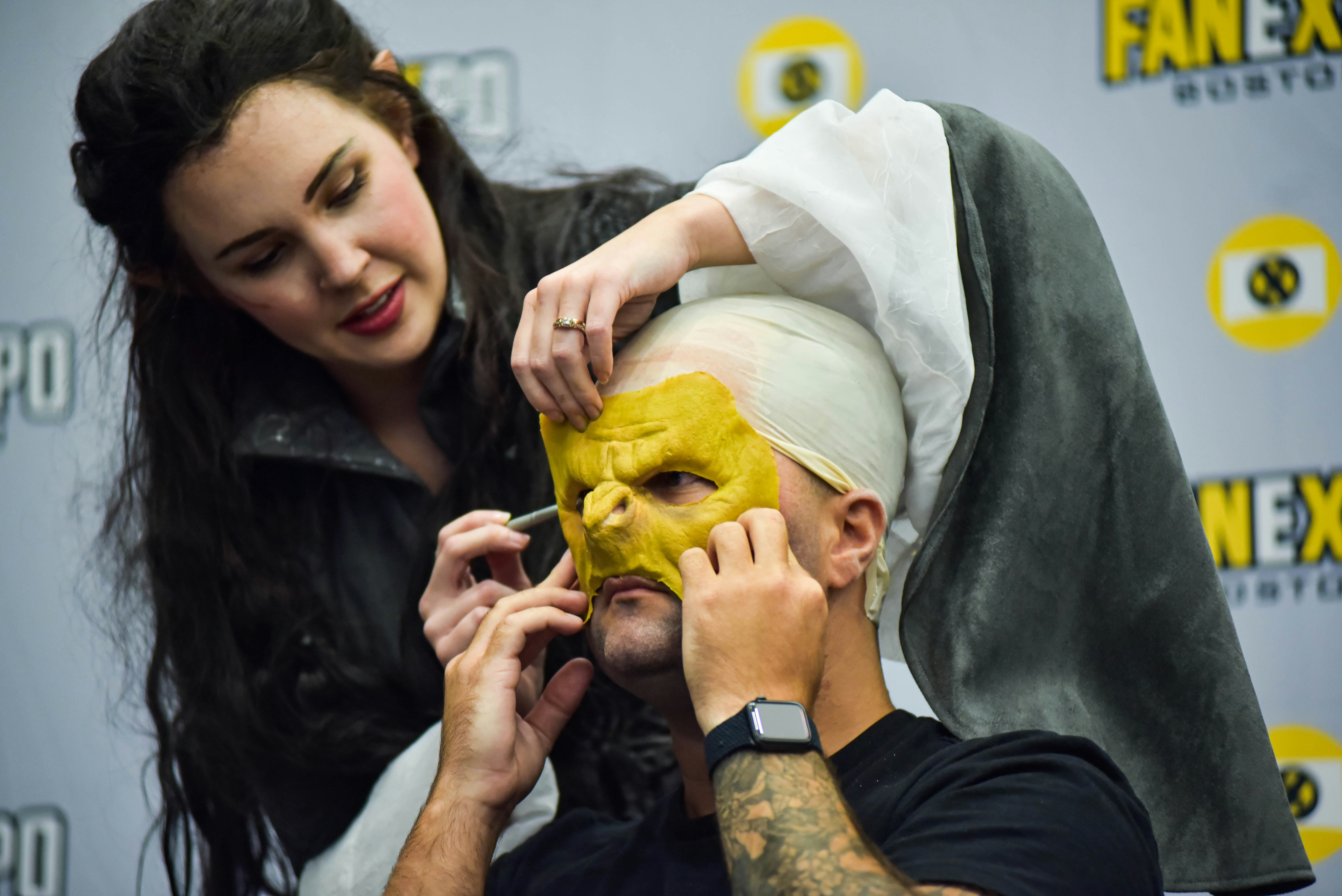 A cosplayer applies makeup and prosthetics live during a panel.